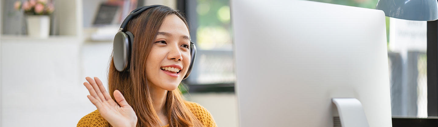 Alt Text for Header Image 	A young female nurse is seated at a table at home participating in an online event. She is smiling and waving hello to the computer camera.