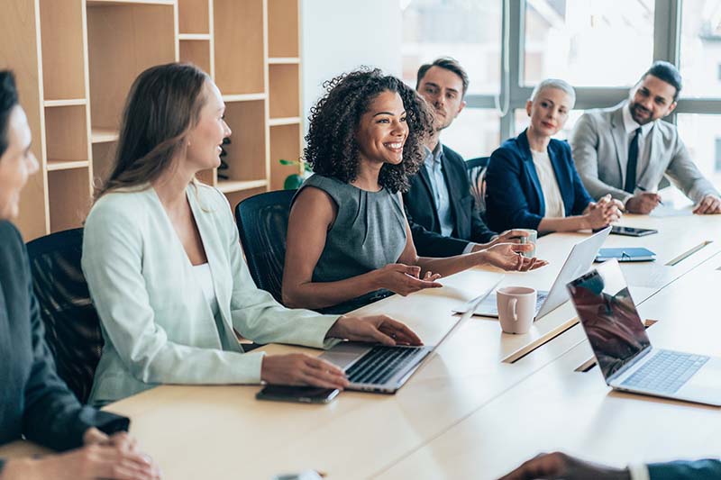 A seated female Director of Nursing is speaking with colleagues while seated at a conference table.