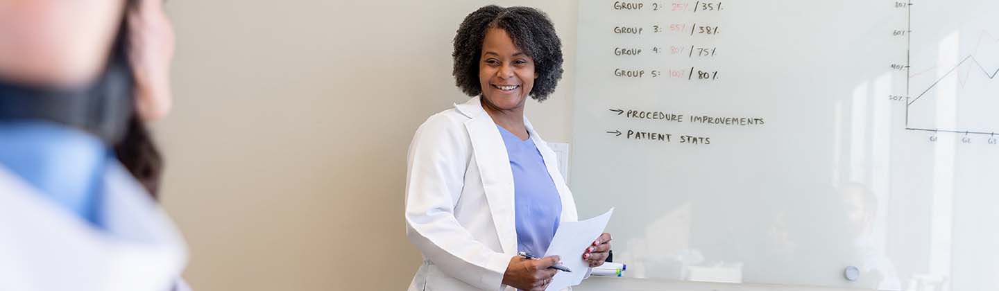 A person in a white coat standing in front of a whiteboard