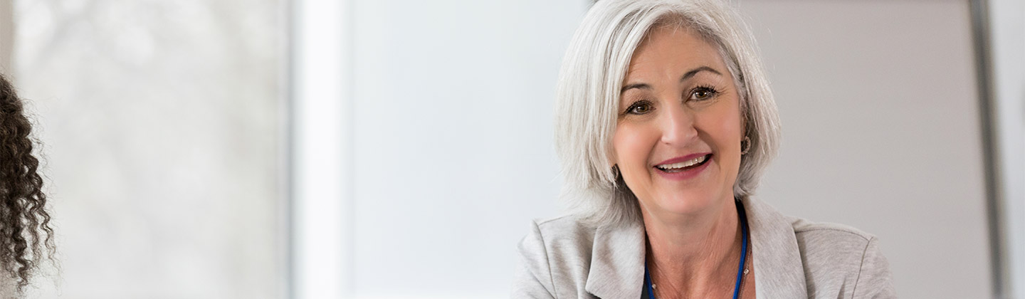 Confident Female Chief Nursing Officer is smiling while seated at a table and meeting with staff members.