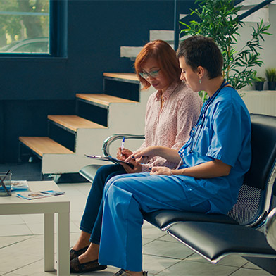 Two nurses, one in scrubs, discuss a patient's chart earnestly, embodying the principle of veracity in nursing through honest communication in a clinic waiting area.